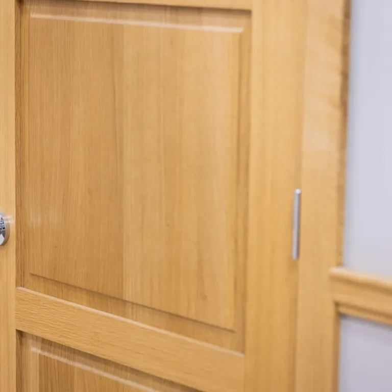 Close-up of a wooden door with a chrome and wood round door knob and light gray wall with wooden trim.