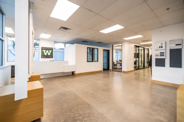 Modern office interior with polished concrete floor, white walls, large windows, wood accents, a reception desk, and glass-walled conference rooms in the background, featuring a Western Pacific logo on one wall.